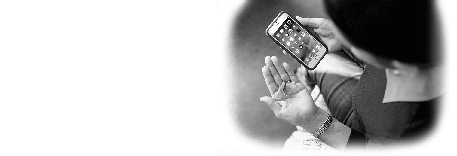 A woman holds her phone and hearing aid.